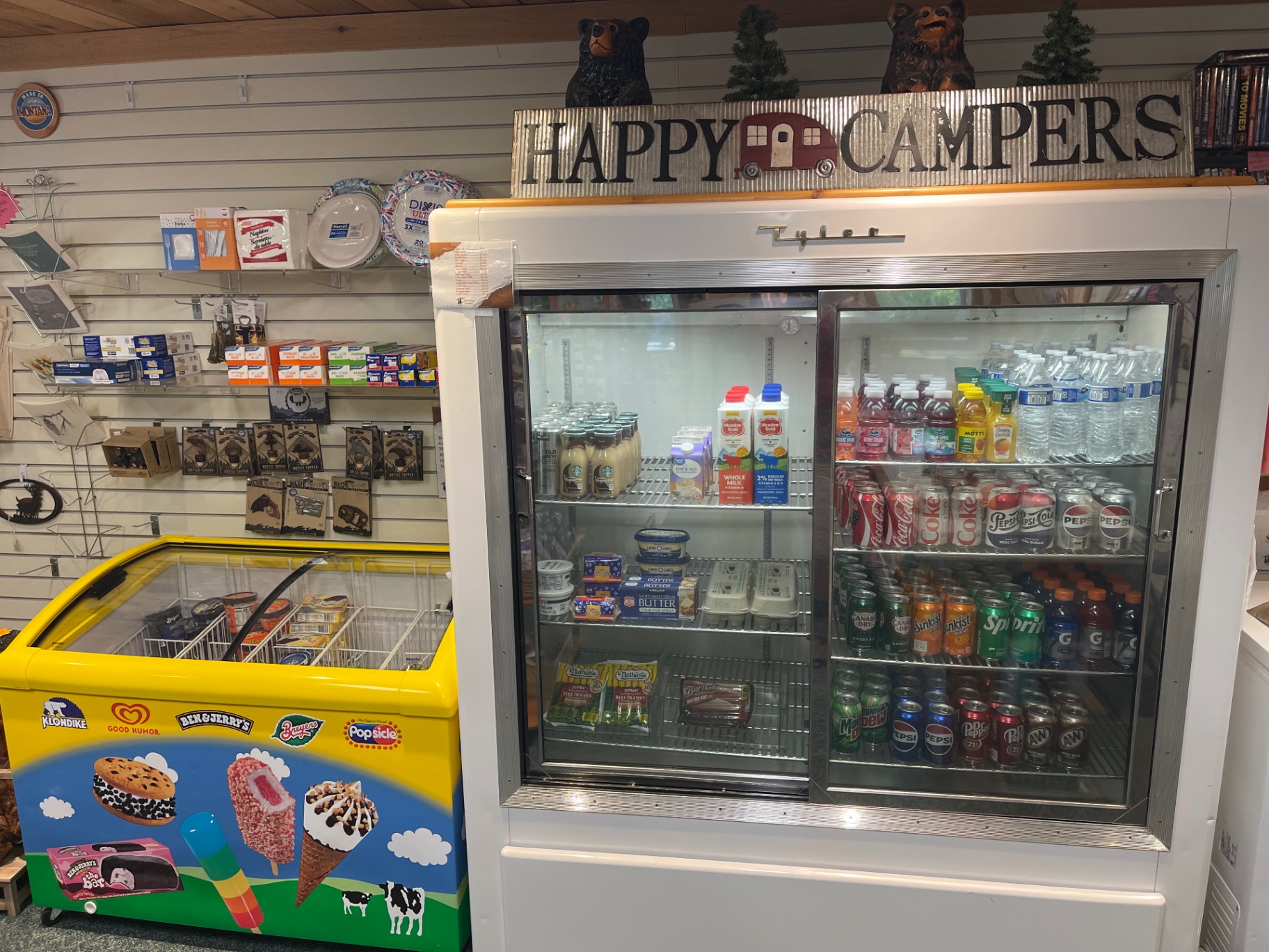 Refrigerated cooler with milk, sodas and water beside a Klondike ice cream freezer under a Happy Campers sign