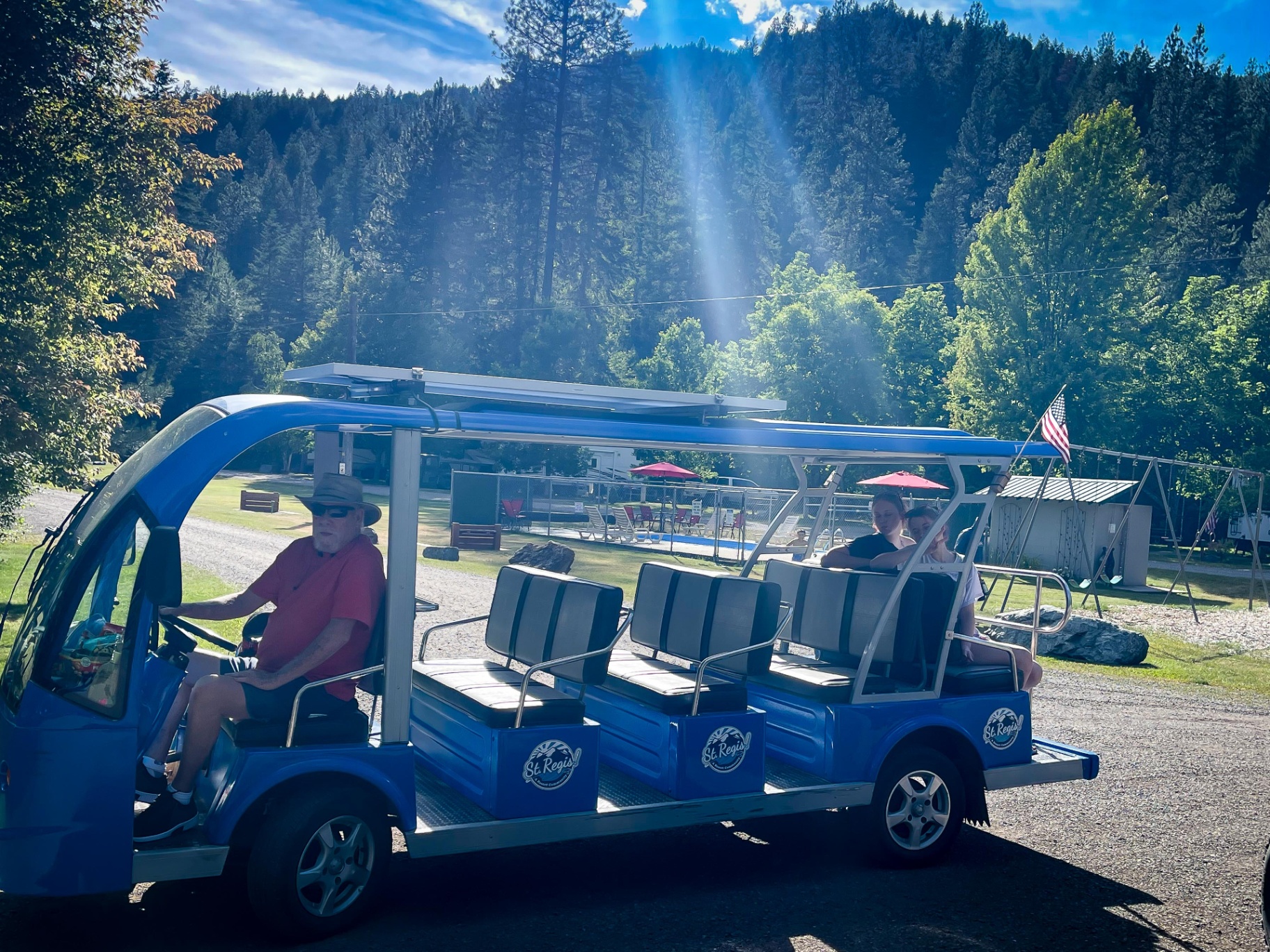 Blue Campground St. Regis shuttle with a driver and guests aboard, with the heated pool and pines in the background