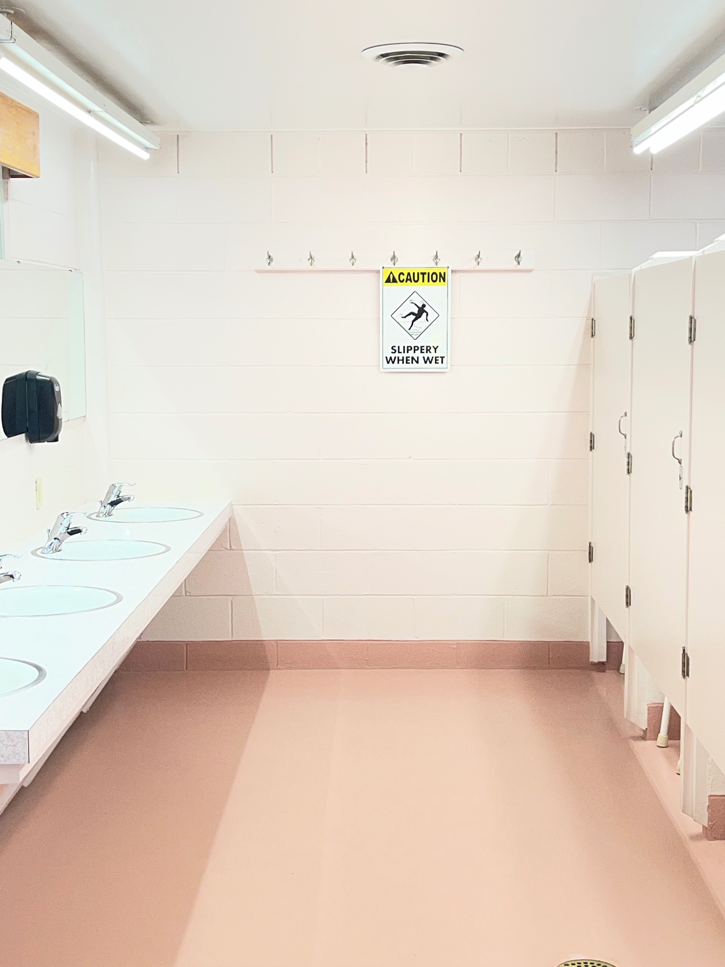 Bright restroom with private stalls, sink counter and soft-pink floors