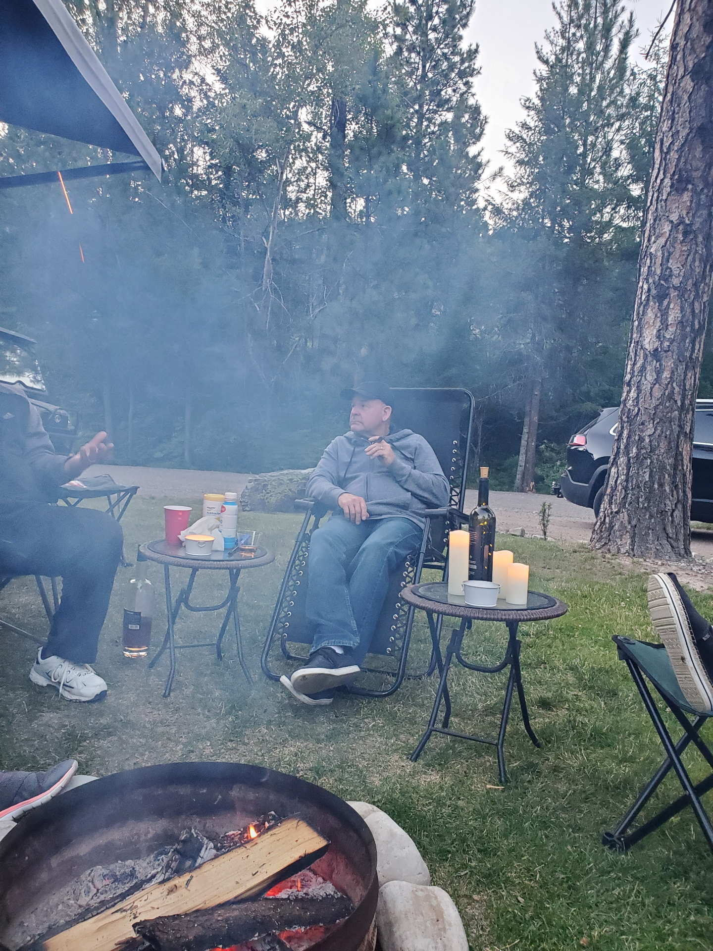 Guests relaxing around an evening campfire under the pines at Campground St. Regis