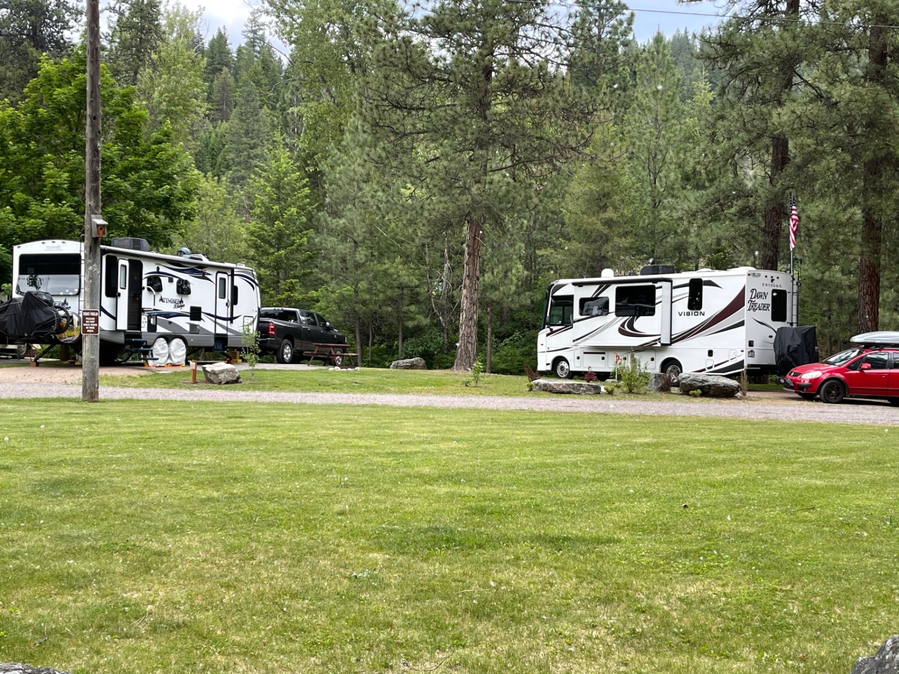 Travel trailer and Class A motorhome on adjacent pull-through sites surrounded by ponderosa pines