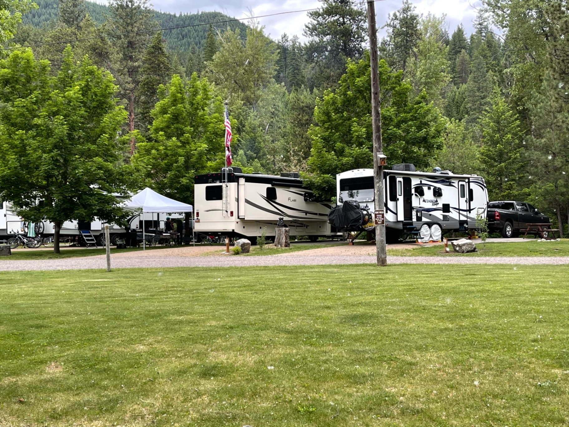 RVs parked on grassy sites with an American flag flying in front of forested Montana mountains