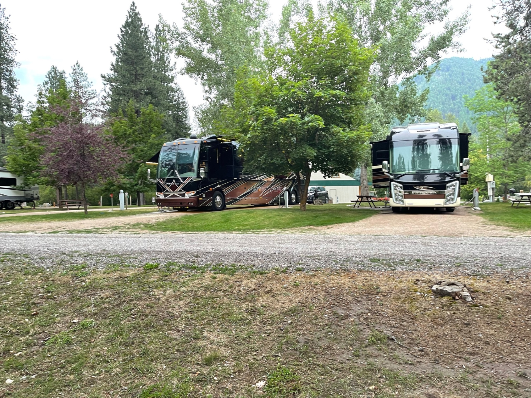 Two high-end diesel pusher motorcoaches parked on open sites with mountain views in the background