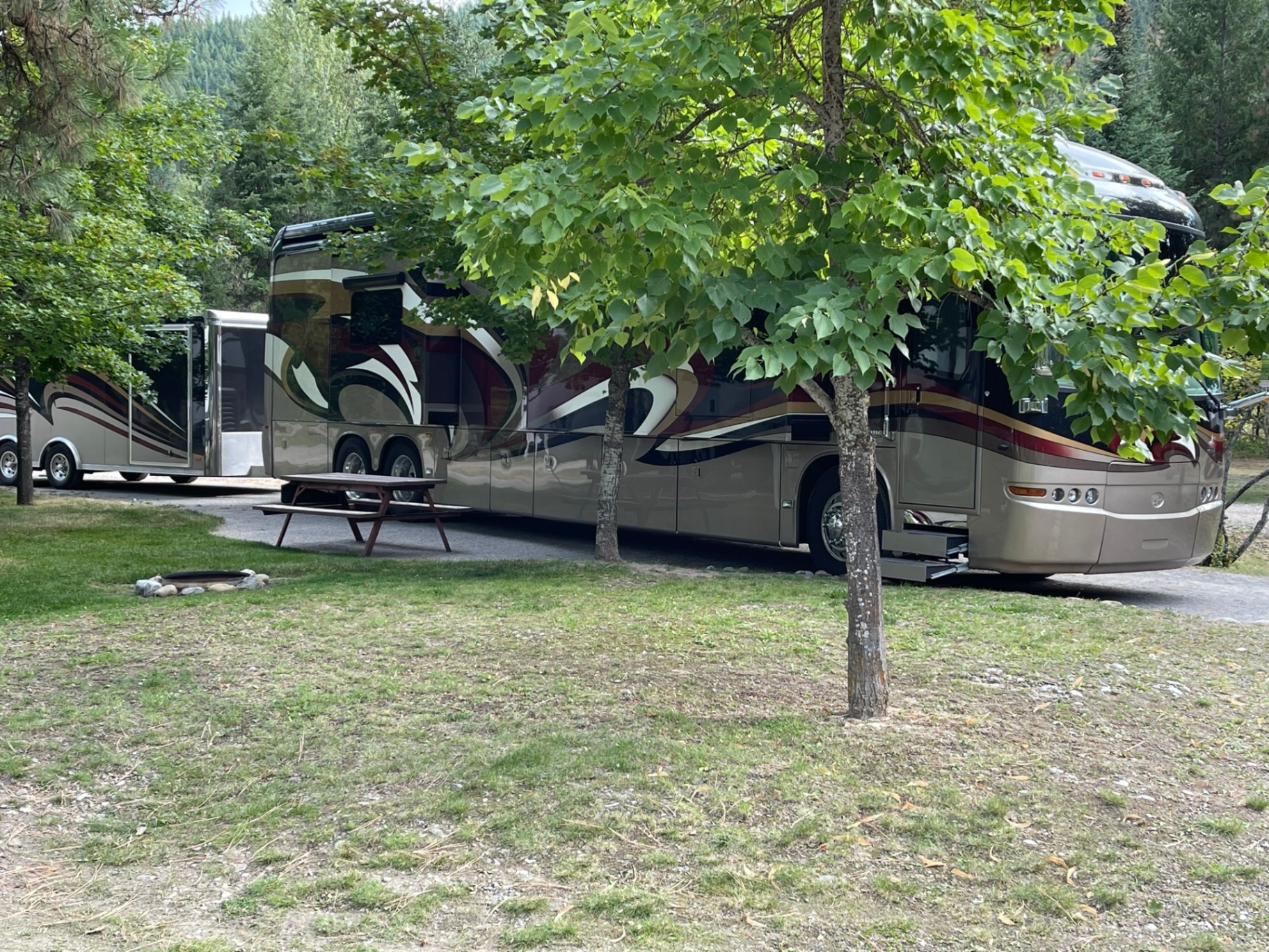 Polished Prevost motorcoach with matching enclosed trailer parked at a shaded pull-through site